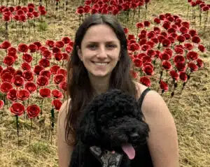A picture of Hannah Read with Tilly the dog sat in front of an art installation of red roses.